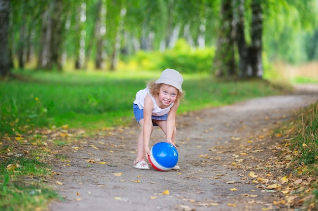 Curly blonde girl jouant avec une balle en caoutchouc dans un parc d'été