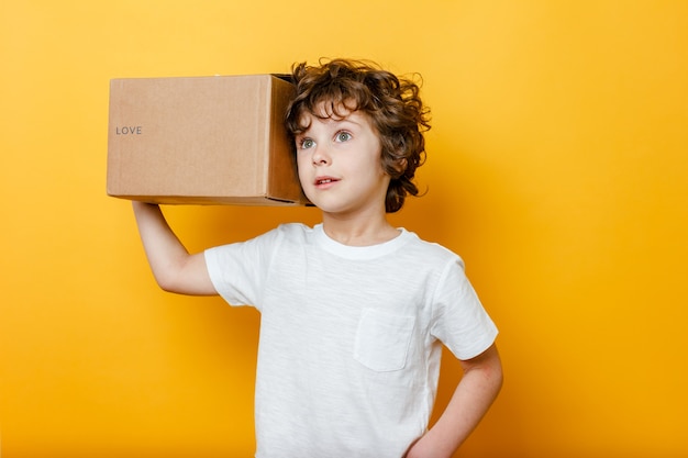 Curly Boy tient une boîte en carton avec le titre LOVE sur son épaule sur jaune