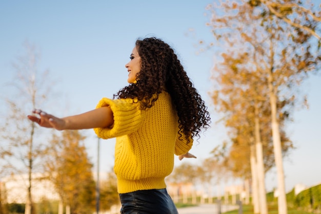 Curly brunette bras tendus soleil souriant dans le parc d'automne