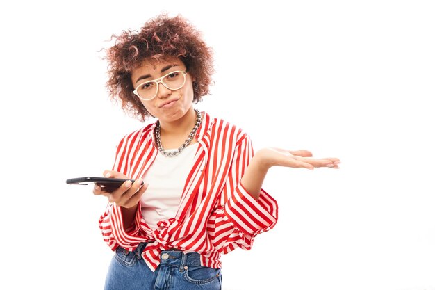 Curly caucasian girl avec expression de visage mécontent holding smartphone isolé sur fond de studio blanc