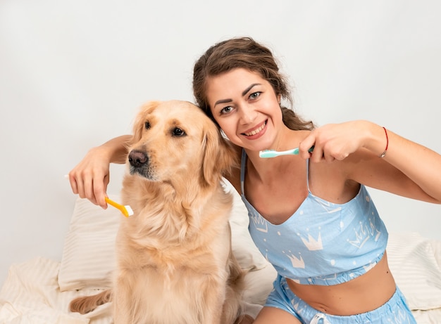 Curly jeune femme en pyjama se prépare à brosser les dents de golden retriever à la maison