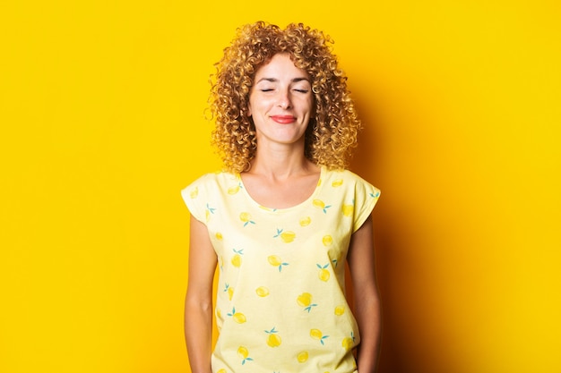 Curly jeune femme souriante avec les yeux fermés sur fond jaune