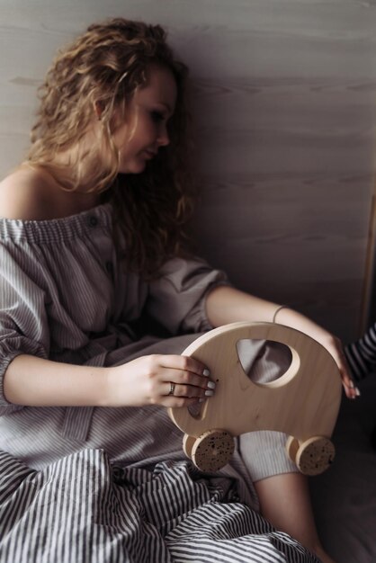 Curly jeune femme vêtue d'une robe tient un jouet en bois dans ses mains