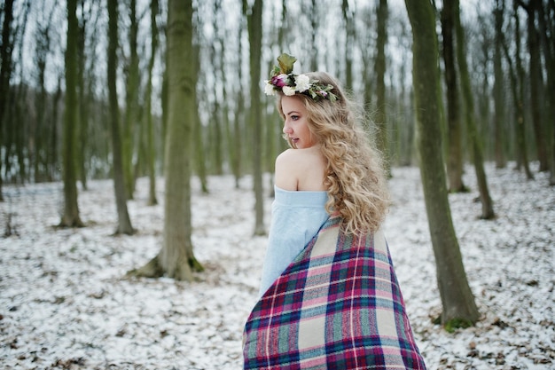 Curly jolie fille blonde avec couronne en plaid à carreaux à la forêt enneigée en journée d'hiver