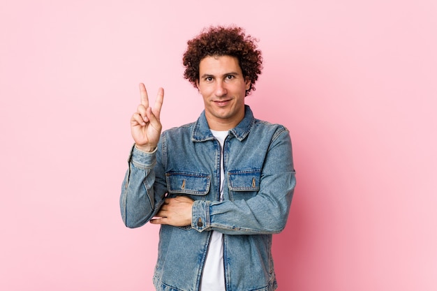 Curly mature man wearing a denim jacket against pink wall montrant le numéro deux avec les doigts.