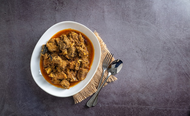 curry de boeuf fait maison dans un bol blanc avec nappe vintage et cuillère ensemble gousses d'ail vue de dessus