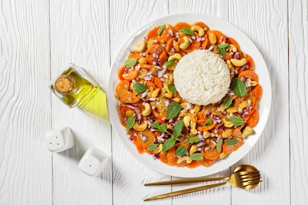 Curry de carottes avec riz basmati sur une assiette blanche sur une table en bois texturée blanche, vue horizontale d'en haut, mise à plat, espace libre, cuisine indienne