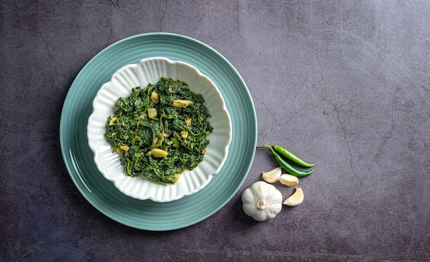 curry d'épinards dans un bol blanc et une assiette bleue avec des piments à l'ail et aux clous de girofle sur une vue de dessus en ardoise noire