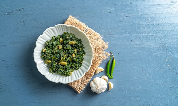 Curry d'épinards de régime alimentaire Keto dans un bol blanc avec des piments à l'ail avec une couche vintage sur une vue de dessus de table en bois bleu