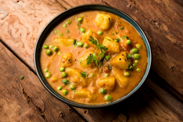 Curry indien Aloo Mutter - Pommes de terre et petits pois immergés dans une sauce à l'oignon et aux tomates et garnis de feuilles de coriandre. Servi dans un Karahi ou un kadhai ou une poêle ou un bol