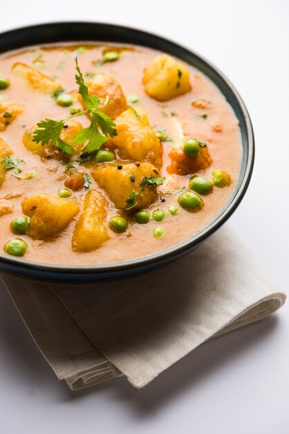 Curry indien Aloo Mutter - Pommes de terre et petits pois immergés dans une sauce à l'oignon et aux tomates et garnis de feuilles de coriandre. Servi dans un Karahi ou un kadhai ou une poêle ou un bol