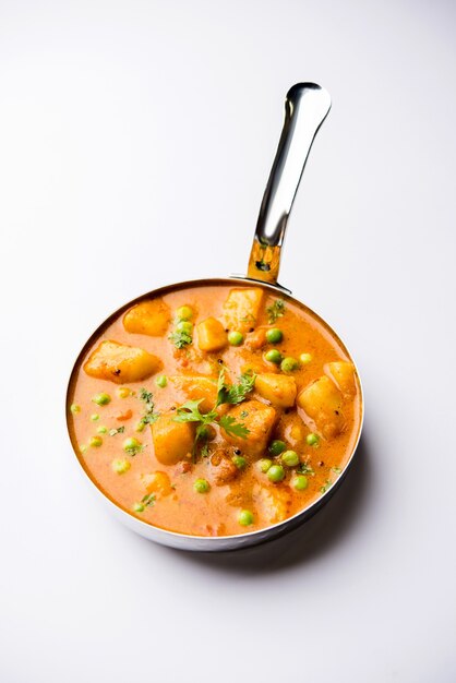 Curry indien Aloo Mutter - Pommes de terre et petits pois immergés dans une sauce à l'oignon et aux tomates et garnis de feuilles de coriandre. Servi dans un Karahi ou un kadhai ou une poêle ou un bol