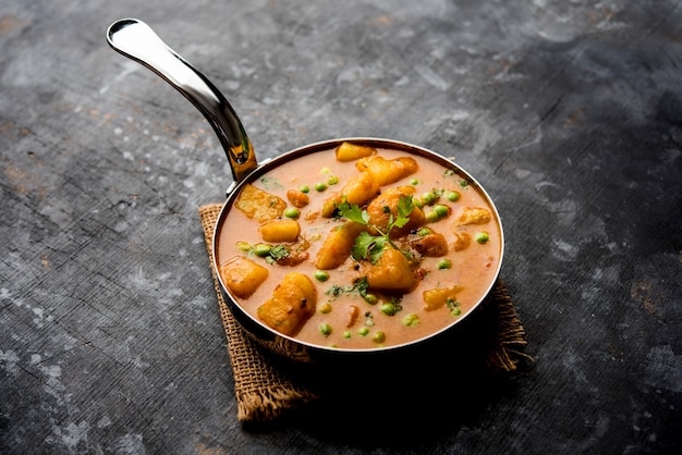 Curry indien Aloo Mutter - Pommes de terre et petits pois immergés dans une sauce à l'oignon et aux tomates et garnis de feuilles de coriandre. Servi dans un Karahi ou un kadhai ou une poêle ou un bol