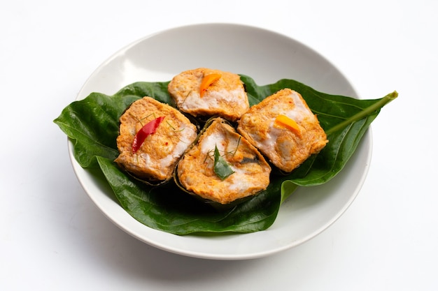 Curry de poisson en streaming thaïlandais dans des feuilles de bananier sur une surface blanche