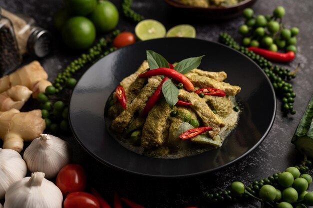 Curry vert de porc dans une assiette noire avec des épices sur un fond de ciment noir