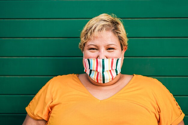 Curvy woman smiling à la caméra tout en portant un masque de protection du visage à l'extérieur