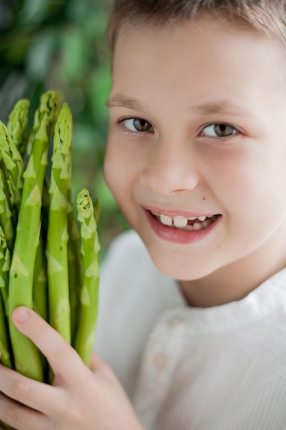 Cute happy fairhaired boy 7 ans est titulaire d'un tas d'asperges vertes juteuses dans ses mains des aliments sains produit Eco Bio