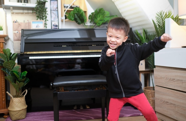 Cute happy smiling little Asian kid boy s'amusant à danser sur de la musique à l'intérieur dans le salon à la maison