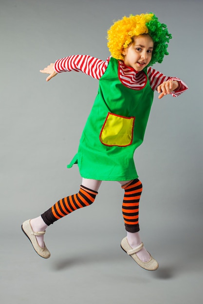 Cute kid clown dans un costume et une perruque de clown Célébration du jour du poisson d'avril Petite fille en drôle de déguisement sur fond gris