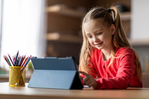 Cute Preteen Girl à l'aide de tablette numérique alors qu'il était assis au bureau à la maison