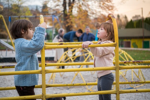 Cutte petite fille et garçon dans un parc pour enfants s'amusant et s'amusant tout en jouant dans une aire de jeux le jour nuageux d'automne