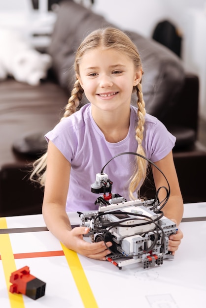 Photo cyber jouet intéressant. sourire joyeux fille amusée assis dans le laboratoire de robotique et tenant un robot cyber tout en exprimant la positivité