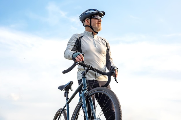 Un cycliste barbu se tient avec un vélo contre le ciel bleu, le cyclisme et les loisirs de santé