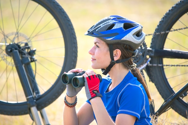 Cycliste de belle fille avec des jumelles à la main sur le vélo. Sports et loisirs