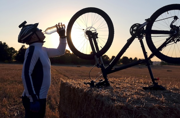 Le cycliste boit de l'eau d'une bouteille contre le soleil couchant