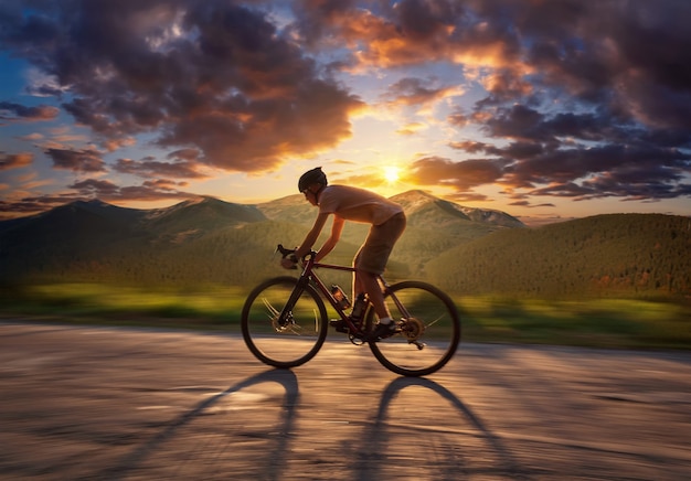 Photo cycliste à cheval sur une route de montagne au coucher du soleil.