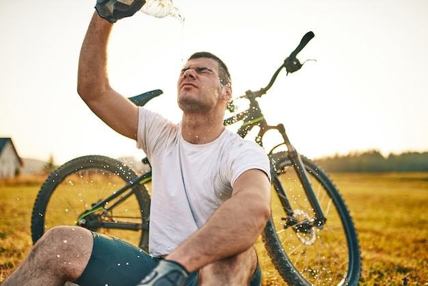 Le cycliste est assis dans un pré tout en se reposant d'une randonnée ardue sur les routes de montagne. Le cycliste est refroidi par l'eau. Mise au point sélective. Photo de haute qualité