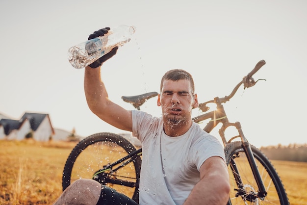 Le cycliste est assis dans un pré tout en se reposant d'une randonnée ardue sur les routes de montagne. Le cycliste est refroidi par l'eau. Mise au point sélective. Photo de haute qualité