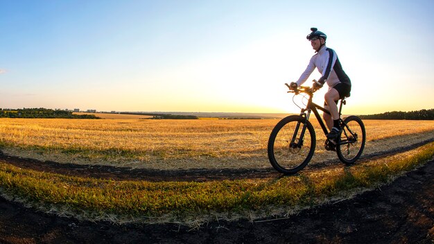 Le cycliste fait du vélo sur la route près du champ sur fond de soleil couchant. Sports de plein air. Mode de vie sain.