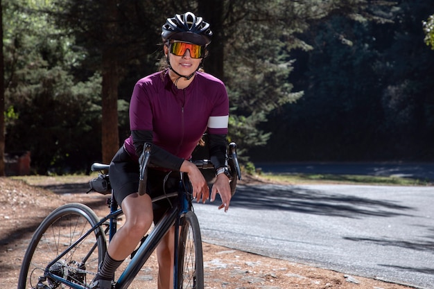 Cycliste latine avec son vélo de piste portant un casque et des lunettes de soleil à côté de la route