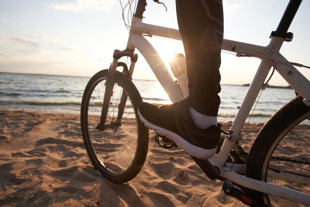 Cycliste masculin conduisant le long d'une plage de sable