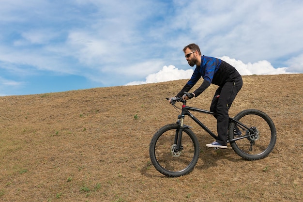 Un cycliste de montagne barbu chevauche des montagnes contre le beau ciel