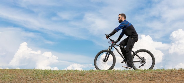 Le cycliste de montagne barbu de panorama monte des montagnes contre le beau ciel