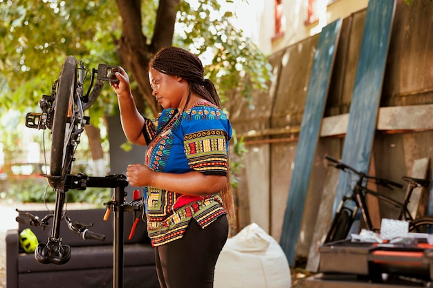 Cycliste noire vérifiant l'équipement dans la cour de la maison dédiée à l'entretien des vélos d'été. Femme afro-américaine sportive dédiée réparant habilement le bras de manivelle de vélo avec des outils professionnels.