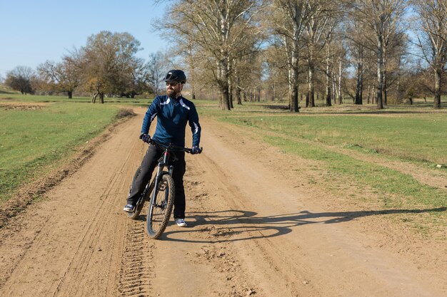 Cycliste en pantalon et veste polaire sur un vélo semi-rigide en carbone moderne avec une fourche à suspension pneumatique roule tout-terrain Le gars se repose sur un banc dans le parc d'automne