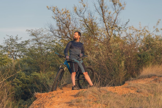 Cycliste en pantalon et veste polaire sur un vélo semi-rigide en carbone moderne avec une fourche à suspension pneumatique roule tout-terrain Le gars se repose sur un banc dans le parc d'automne