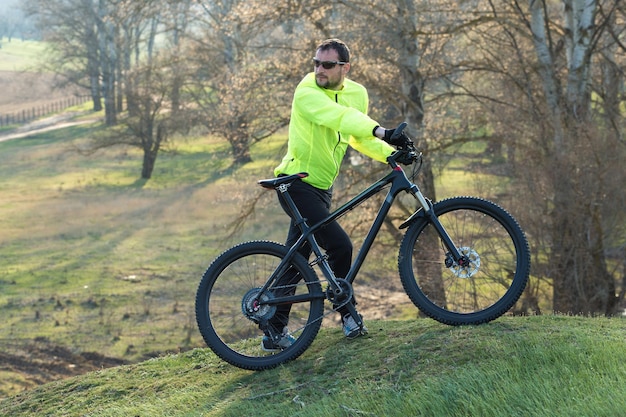 Cycliste en pantalon et veste verte sur un vélo semi-rigide moderne en carbone avec fourche à suspension pneumatique