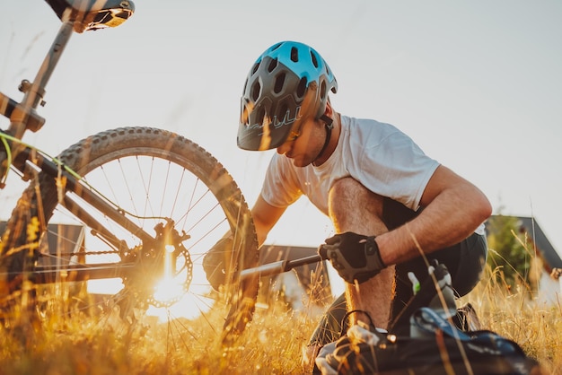 Le cycliste répare et change le pneu de son vélo à la montagne au coucher du soleil. Réparation de pneus de vélo. Mise au point sélective. Photo de haute qualité