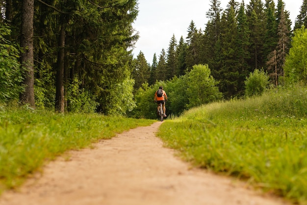 Le cycliste avec un sac à dos sur des promenades en VTT le long d'un chemin forestier