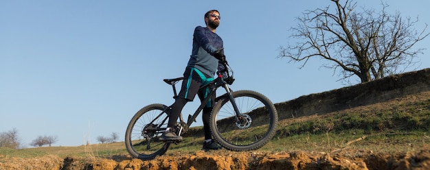 Cycliste en short et maillot sur un vélo semi-rigide en carbone moderne avec une fourche à suspension pneumatique debout sur une falaise sur fond de forêt printanière verte fraîche