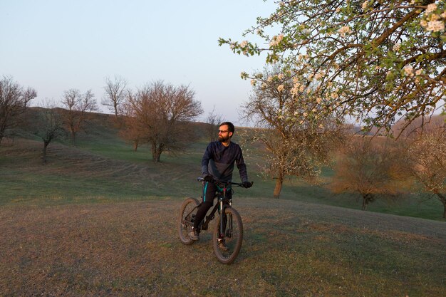 Cycliste en short et maillot sur un vélo semi-rigide moderne en carbone avec une fourche à suspension pneumatique debout sur une falaise sur fond de forêt printanière verte et fraîche