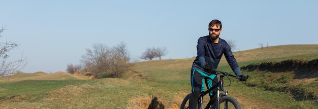 Cycliste en short et maillot sur un vélo semi-rigide moderne en carbone avec une fourche à suspension pneumatique debout sur une falaise sur fond de forêt printanière verte et fraîche