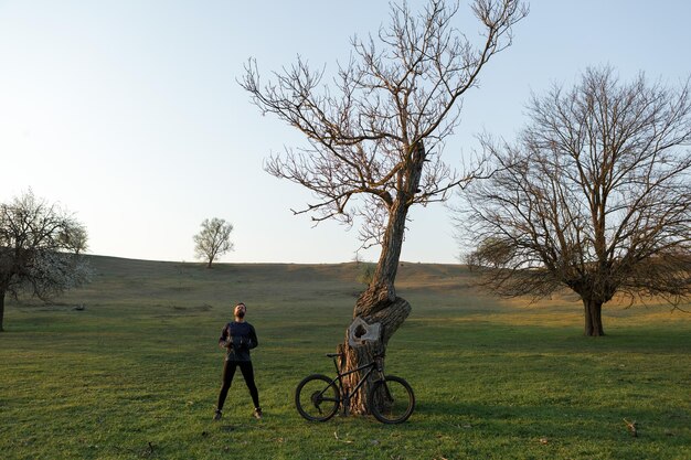 Cycliste en short et maillot sur un vélo semi-rigide moderne en carbone avec une fourche à suspension pneumatique debout sur une falaise sur fond de forêt printanière verte et fraîche