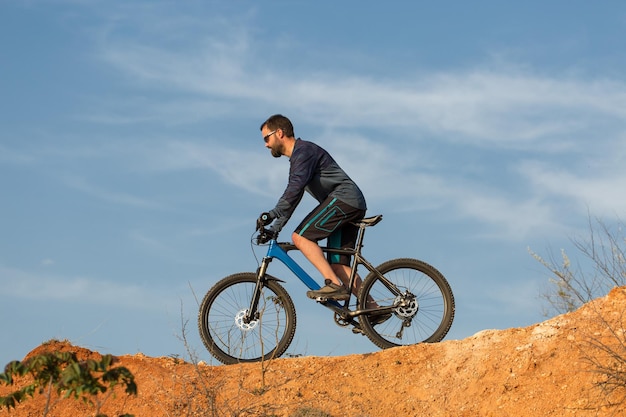 Cycliste en short et maillot sur un vélo semi-rigide moderne en carbone avec une fourche à suspension pneumatique debout sur une falaise sur fond de forêt printanière verte et fraîche