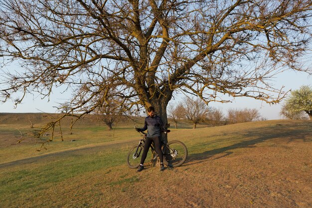 Cycliste en short et maillot sur un vélo semi-rigide moderne en carbone avec une fourche à suspension pneumatique debout sur une falaise sur fond de forêt printanière verte et fraîche