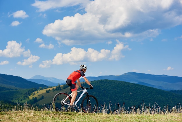 Cycliste sportif professionnel équitation vélo de cross-country en haute colline herbeuse. Belle vue sur les montagnes et ciel nuageux sur fond